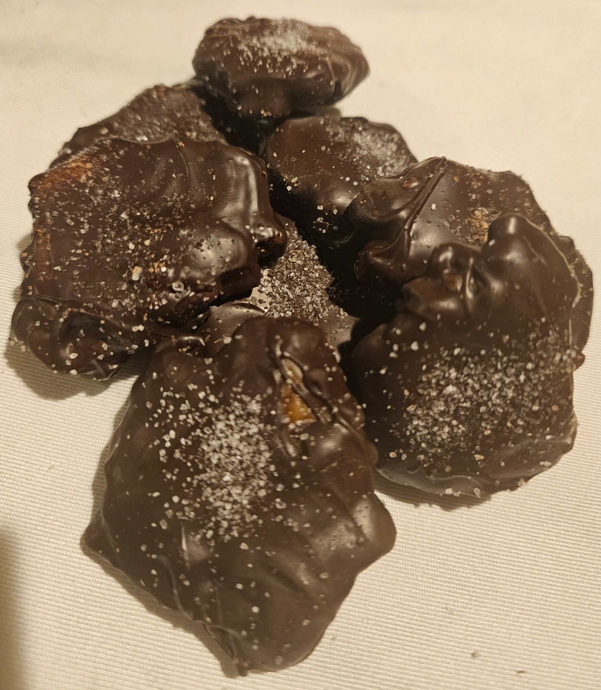 Hand-dipped caramel pecan clusters with sea salt on smooth chocolate in a white box